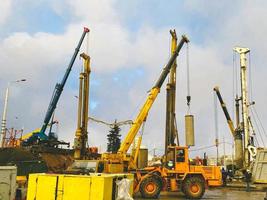 equipo de construcción en el sitio de reparación del paso elevado. una grúa amarilla alta con ruedas grandes lleva un bloque de hormigón redondo, una pila para la construcción de un gran paso elevado foto