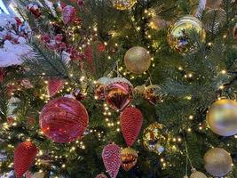 Green branches of a fluffy Christmas festive New Year tree with toys in balls and bright glowing light bulbs and garlands, background photo