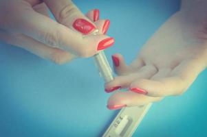 finger puncture to diagnose coronavirus. girl with red manicure makes herself an analysis on her own. the girl holds a lancet and pricks her finger with the second hand photo