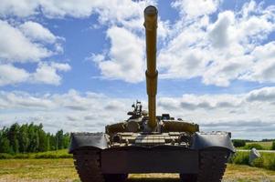 A large green military metal armored deadly dangerous iron Russian Syrian battle tank with a gun turret and a goose is parked parked against a blue sky and clouds outside the city photo