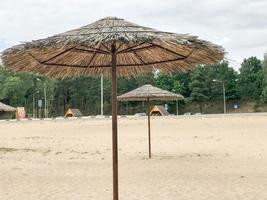 una playa desierta vacía con mal tiempo, otoño frío fuera de temporada con sombrillas de paja contra el cielo azul foto