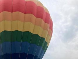 Large multi-colored bright round rainbow colored striped striped flying balloon with a basket against the sky in the evening photo