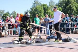 A fireman in a fireproof suit and a helmet running with an oxygen balloon pulling, holding a fire hose at a fire sport competition. Minsk, Belarus, 08.07.2018 photo