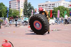 A fireman in a fireproof suit and a helmet runs and turns a large rubber wheel in a fire fighting competition, Belarus, Minsk, 08.08.2018 photo