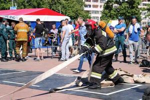 A fireman in a fireproof suit and a helmet running with an oxygen balloon pulling, holding a fire hose at a fire sport competition. Minsk, Belarus, 08.07.2018 photo