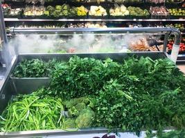 Green fresh environmentally friendly greens of parsley plants dill salad arugula onions and other plant foods lies in a modern refrigerator in a supermarket store on the counter. The background photo