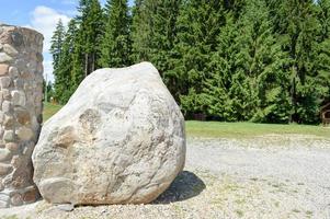 gran roca de piedra natural adoquín gris sólido gigante yace en el suelo junto a la columna contra el fondo de árboles verdes foto