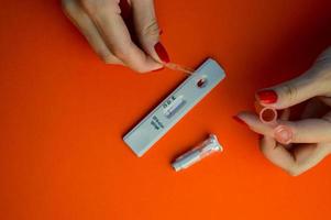 test for coronavirus on an orange background. a sensitive strip, a girl with a bright red manicure drips onto a drop of blood for a test and adds a physical solution there, a lancet lies nearby photo