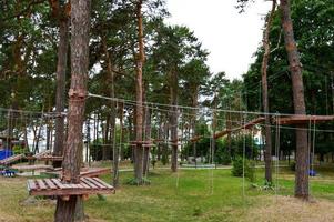 A climbing wall, trolls and a rope park are sporting for games and entertainment from boards and trees with ropes for playing children and adults in the woods in nature photo