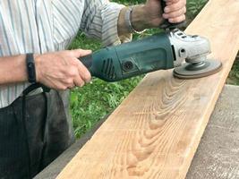 el hombre trabaja con sus manos, muele el disco para el molinillo, la herramienta eléctrica para moler y pulir la superficie de la tabla de madera foto