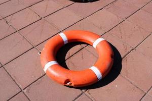 A large round orange plastic life ring for safety and rescue people in the water lies on the stone floor photo