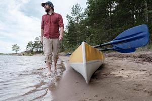 A happy, smiling man parked his kayak and walks barefoot on the water of the lake, enjoying the beautiful views. photo