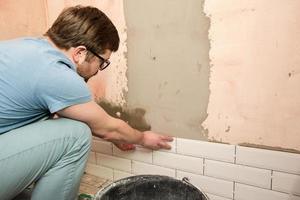 Focused tiler is laying tiles on the bathroom wall. Home repairs. photo