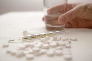 Medical thermometer, with a temperature of 37 degrees, lies in a pile of pills, in the background a hand takes a glass of water. photo