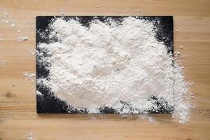 Flour sprinkled on a slate cutting board that is on a wooden table. Copy space. photo