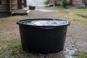 Rainwater is collected in a basin of standing under the gutter, in the yard, on a summer day. photo