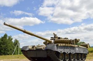 A large green military metal armored deadly dangerous iron Russian Syrian battle tank with a gun turret and a goose is parked parked against a blue sky and clouds outside the city photo