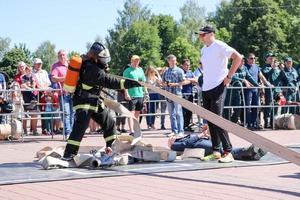 A fireman in a fireproof suit and a helmet running with an oxygen balloon pulling, holding a fire hose at a fire sport competition. Minsk, Belarus, 08.07.2018 photo