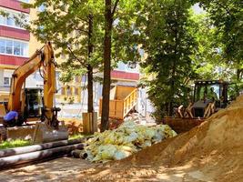 tendido de comunicaciones en el patio. la excavadora excava agujeros para colocar tuberías de plomería. cerca hay materiales de construcción en bolsas selladas foto