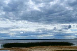 vista panorámica del lago con agua y plantas en la orilla, juncos y sombrías nubes azules en el cielo foto