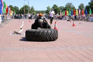 A fireman in a fireproof suit and a helmet runs and turns a large rubber wheel in a fire fighting competition, Belarus, Minsk, 08.08.2018 photo