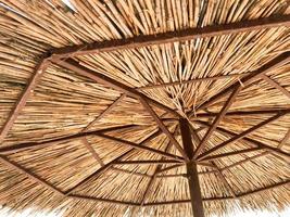 Texture of a natural straw dry beach sun umbrella made from hay dried grass and branches on the beach against a blue sky at a rest resort photo