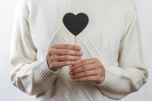 chica sosteniendo un tablero de corazón negro sobre fondo blanco, día de san valentín foto