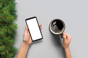 Female hands holding black mobile phone with blank white screen and mug of coffee. Mockup image with copy space. Top view on purple background, flat lay photo