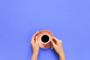 Minimalistic style woman hand holding a cup of coffee on purple background. Flat lay, top view photo