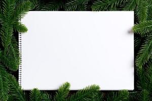 Top view of notebook decorated with a frame made of fir tree on wooden background. New Year time concept photo