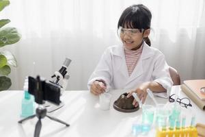 Asian school girl making easy chemistry experiments and recording a video for his followers, Young blogger kid posing in front of camera for vlog, Children make vlog for social media channel concept. photo