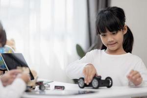 dos estudiantes asiáticos aprenden a codificar autos robot y cables de tableros electrónicos en tallo, vapor, ingeniería matemática, ciencia, tecnología, código de computadora en robótica para conceptos de niños. foto