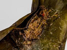 Botok Indonesian traditional Javanese food. Botok is made from grated coconut, anchovies, mlanding, tempe then wrapped in banana leaves and steamed. Presented on a white background photo