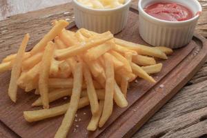 French fries in cutting board has mayonnaise and tomato sauce on wood background unhealthy food concept. photo