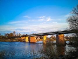 Ancient bridge over the river with stone pillars. Rapid flow of water in spring. Sunset view. photo