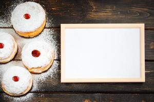 Happy Hanukkah. Empty frame for congratulations text and traditional dessert Sufganiyot on dark wooden background. Celebrating Jewish holiday. photo