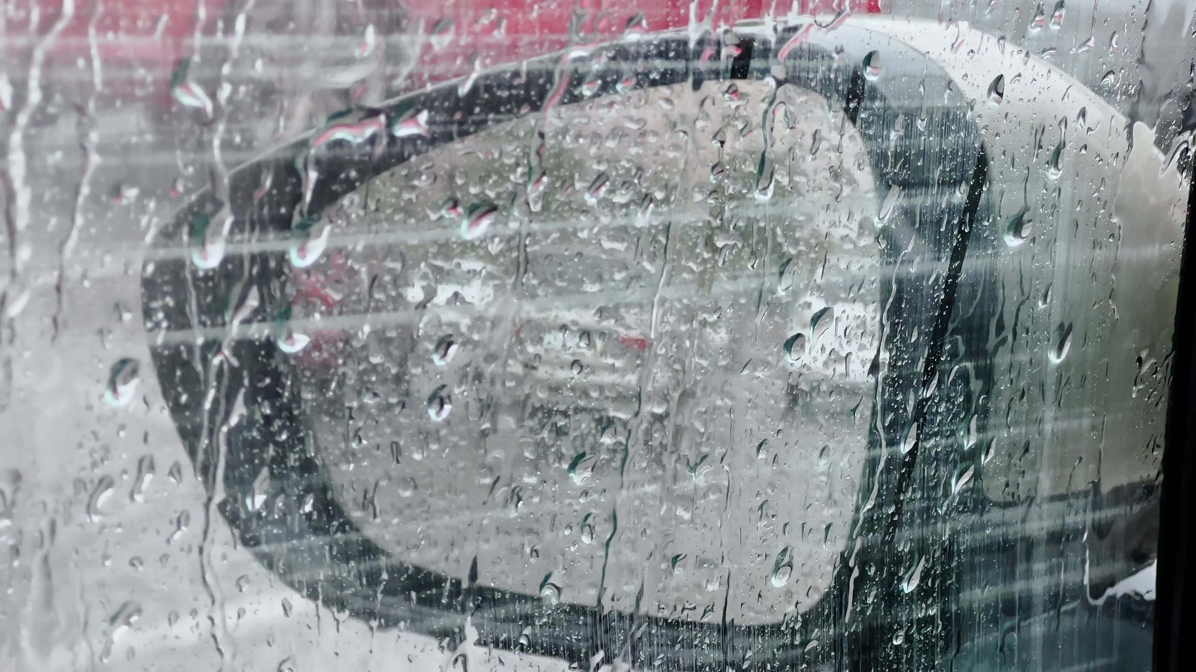 Heavy rain, drops falling on car window through which side mirror is