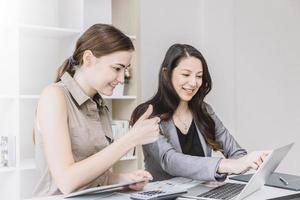 two business girls working good job thumb up at office desk with laptop photo