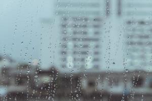 lloviendo en el cristal de las ventanas con el fondo del edificio de la ciudad borrosa foto