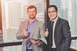 Asian and Caucasian Business man standing thumbs up and happy smile for job done in office for good job concept. photo