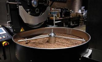 Coffee roaster machine at coffee roasting process. Mixing coffee beans. Roasted spinning cooler professional machines and fresh brown coffee beans movement close-up dark photo at factory.