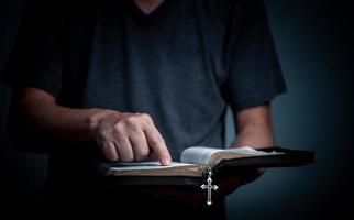 Young man reading Holy Bible and pointing on the word with cross necklace in font of the book. photo