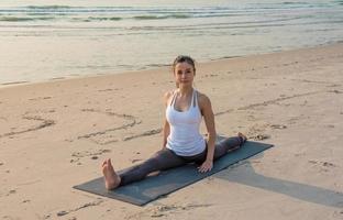 joven asiática sana haciendo ejercicio de yoga en la playa por la mañana. foto