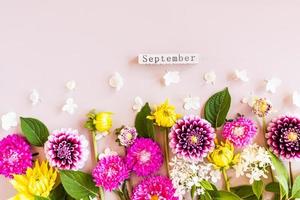 autumn bright cut flowers in a floral composition on a beige background. flat lay. top view. wooden calendar-September.