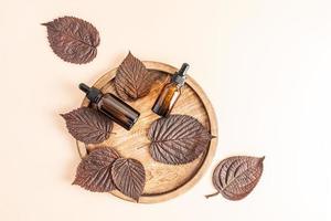vista superior de dos botellas con un medio activo para rejuvenecer la piel de la cara en una bandeja redonda de madera con hojas de otoño. cosméticos orgánicos. foto