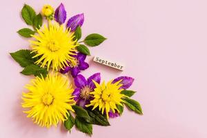 top view of the wooden calendar with September word and yellow dahlias, purple clematis. pastel background. a copy of the space. photo