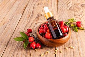 a bottle dropper with a cosmetic based on rosehip sea oil for facial skin care lies in a wooden bowl with berries. anti-aging care photo