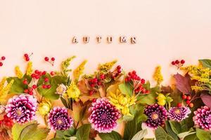 beautiful bright border of autumn flowers, leaves and berries. beige background. the inscription is autumn made of wooden letters. postcard. poster. photo