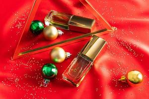 a cosmetic bottle of toilet water lies on a mirror with Christmas glass balls. red fabric satin background. advertising concept. photo