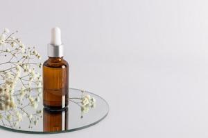 a cosmetic bottle with an amber glass dropper with an eco-natural remedy stands on a round mirror. an empty layout of a cosmetic brand. a copy space. photo